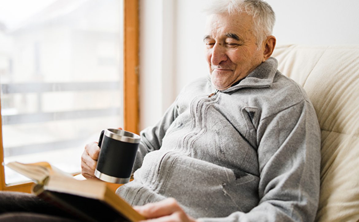 Senior man old sitting and Reading a book at the retirement nursing home with cup of tea in hand